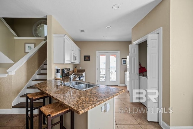 kitchen with a breakfast bar, white cabinets, light tile floors, electric range, and sink