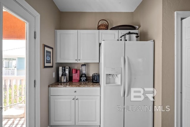 kitchen featuring white cabinets, white fridge with ice dispenser, and dark stone counters