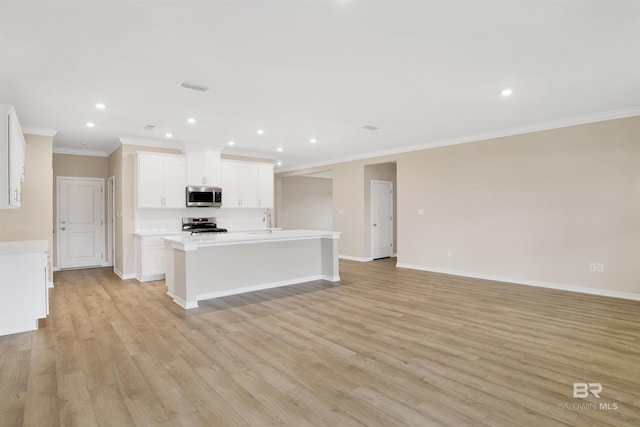 kitchen with stainless steel appliances, light wood-style flooring, a center island with sink, crown molding, and light countertops