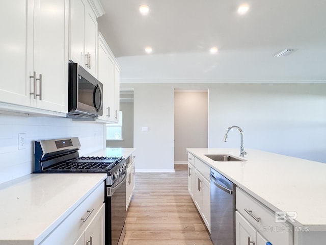 kitchen featuring light wood finished floors, stainless steel appliances, backsplash, a sink, and crown molding