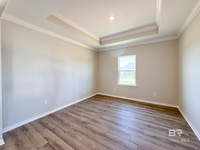 empty room featuring baseboards, crown molding, wood finished floors, and a raised ceiling
