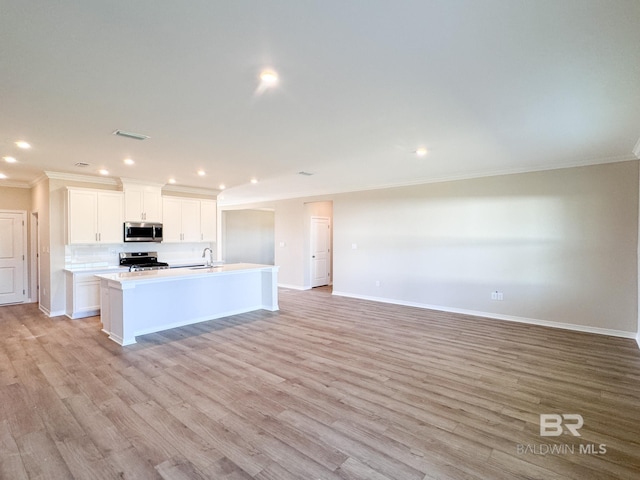 kitchen featuring stainless steel appliances, ornamental molding, a sink, a center island with sink, and baseboards