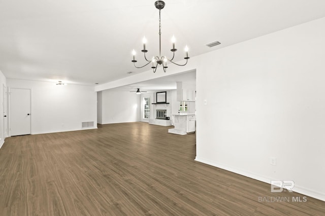 unfurnished living room with ceiling fan with notable chandelier and dark wood-type flooring