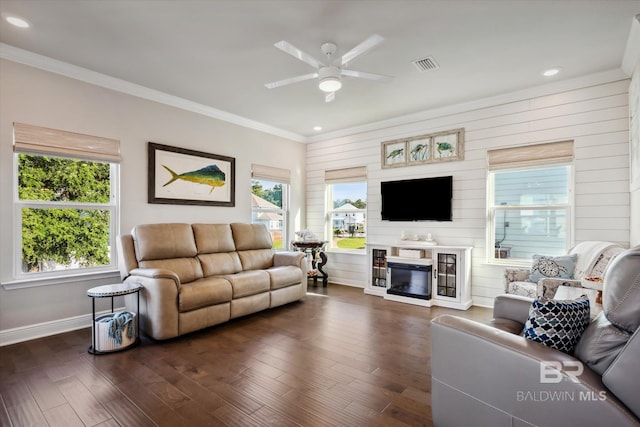 living room with wood walls, dark wood-type flooring, ceiling fan, and ornamental molding