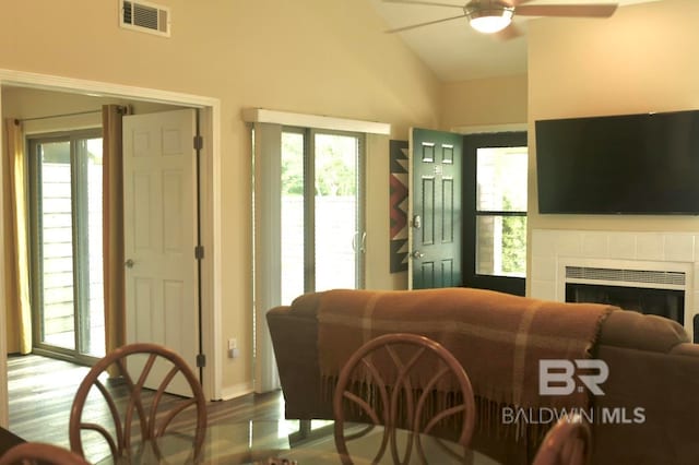 living room with wood-type flooring, ceiling fan, a tile fireplace, and lofted ceiling