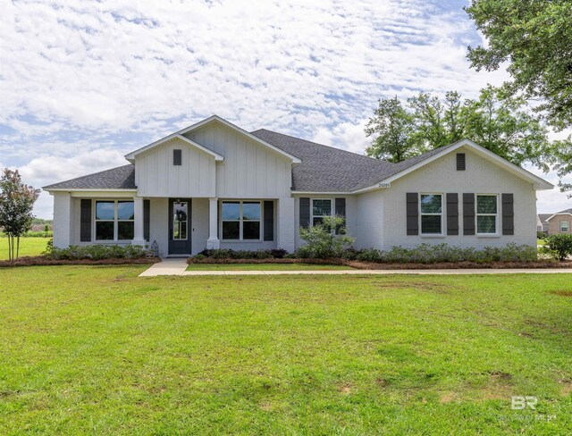 view of front of home with brick siding, a front lawn, board and batten siding, and a shingled roof
