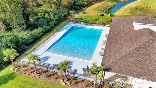 pool with a patio, a water view, fence, and a yard