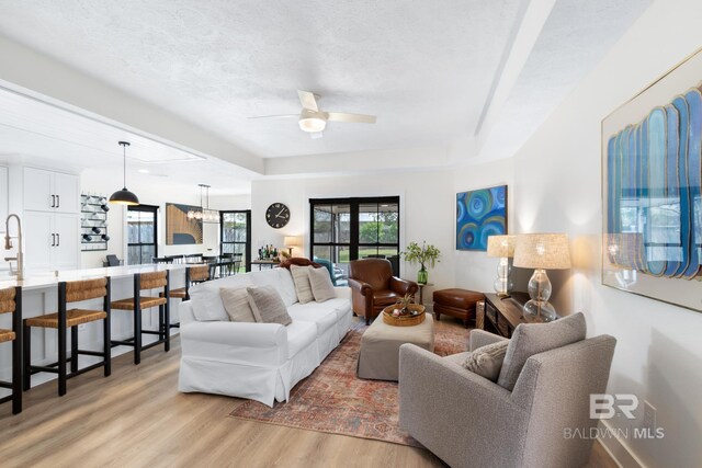 5100 Pine Way, Orange Beach, AL 36561 - living room with light wood-type flooring, a ceiling fan, a textured ceiling, and a raised ceiling