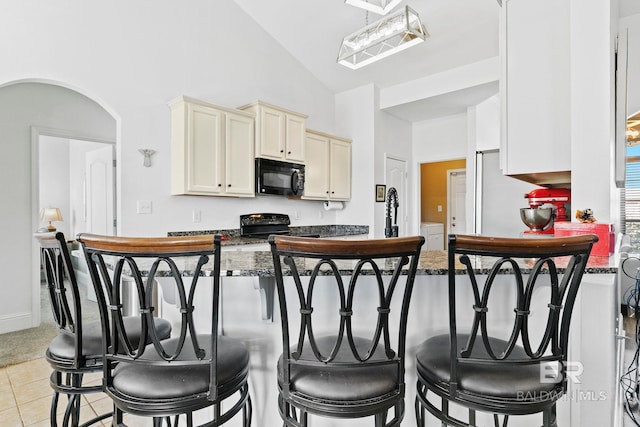 kitchen featuring lofted ceiling, a kitchen breakfast bar, dark stone counters, light tile patterned floors, and black appliances