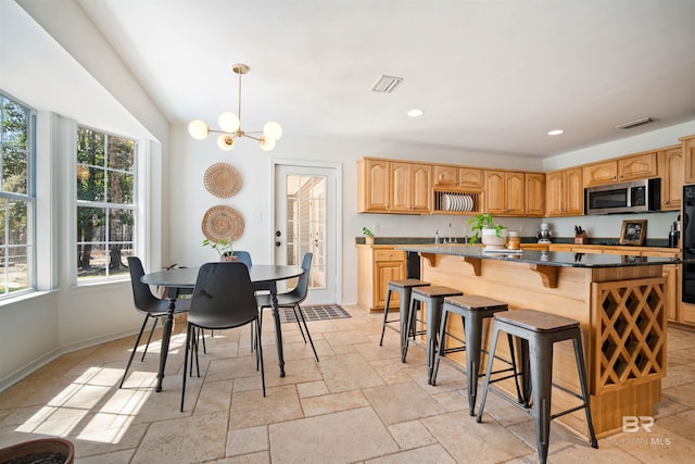 kitchen featuring visible vents, a kitchen island, stone tile flooring, stainless steel microwave, and a kitchen breakfast bar