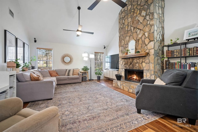 living room featuring a stone fireplace, plenty of natural light, wood finished floors, and visible vents