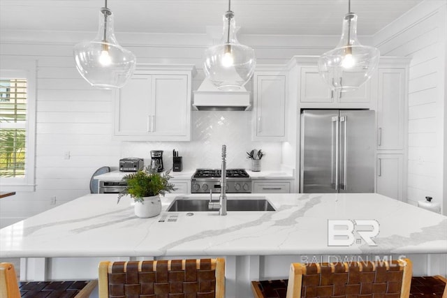 kitchen with light stone counters, high end fridge, a kitchen island with sink, and white cabinetry