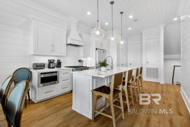 kitchen featuring visible vents, wood ceiling, an island with sink, light countertops, and custom range hood