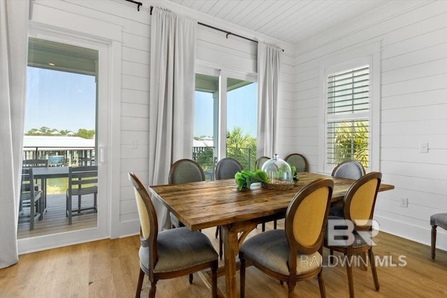 dining space with wooden walls, a healthy amount of sunlight, and light wood finished floors