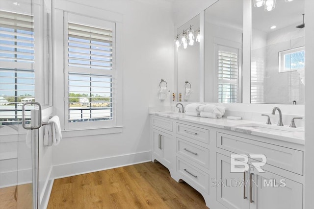 bathroom with double vanity, wood finished floors, a shower with shower door, and a sink