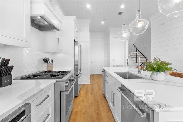 kitchen with custom range hood, a sink, premium appliances, light wood-style floors, and white cabinets