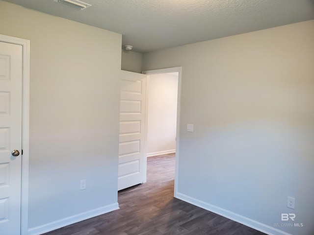 unfurnished room featuring dark wood-type flooring and a textured ceiling