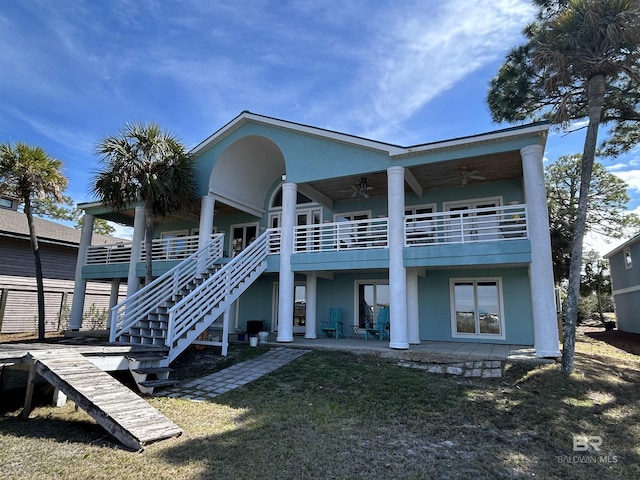 rear view of property with a lawn, a ceiling fan, a patio, stairway, and stucco siding