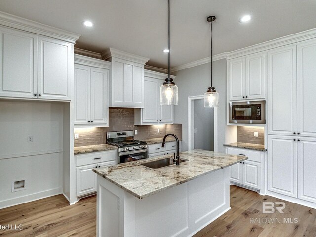 kitchen with built in microwave, stainless steel range with gas stovetop, light wood-type flooring, white cabinets, and a sink