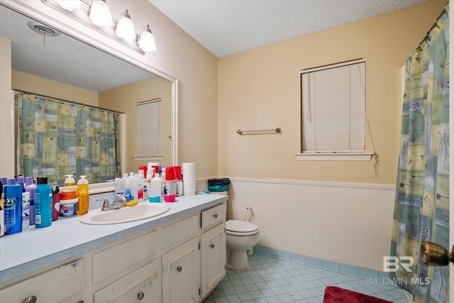 bathroom featuring vanity, toilet, wainscoting, and a textured ceiling