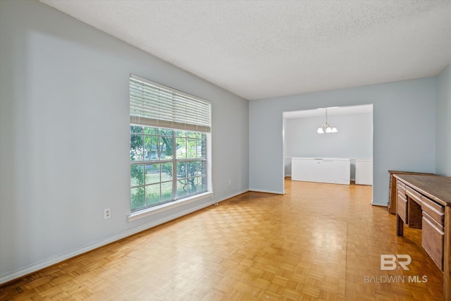 spare room with light parquet floors, an inviting chandelier, and a textured ceiling