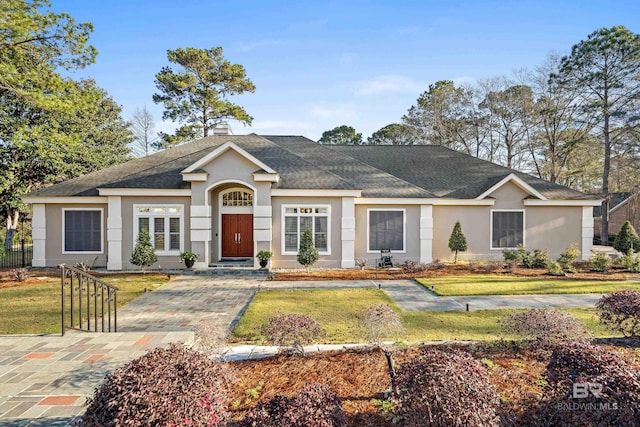 single story home featuring stucco siding, a chimney, a front yard, and a shingled roof