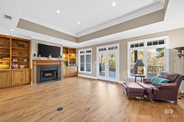 living room featuring visible vents, crown molding, light wood-type flooring, and a raised ceiling