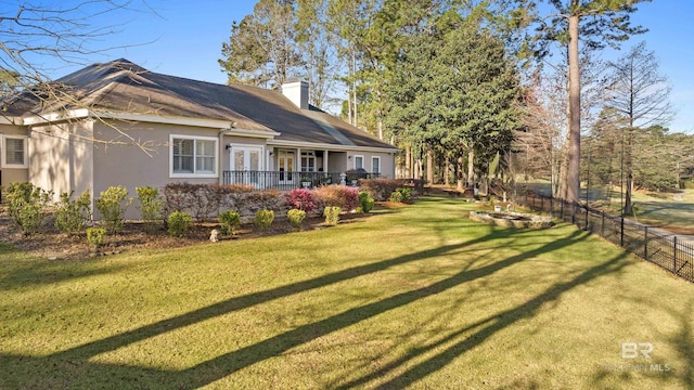 rear view of house featuring stucco siding, a lawn, fence, french doors, and a chimney