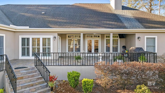 view of exterior entry featuring stucco siding, french doors, a chimney, and a shingled roof