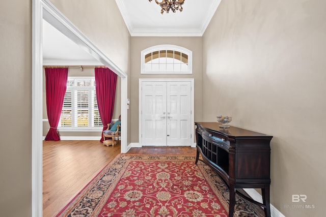 entrance foyer with a chandelier, wood finished floors, baseboards, and ornamental molding