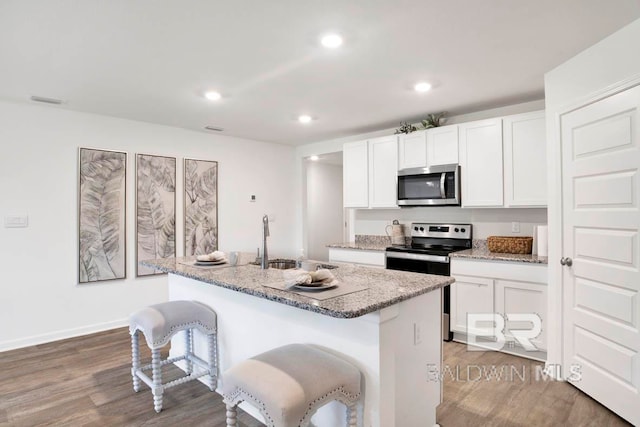 kitchen with light stone counters, hardwood / wood-style floors, an island with sink, white cabinetry, and appliances with stainless steel finishes