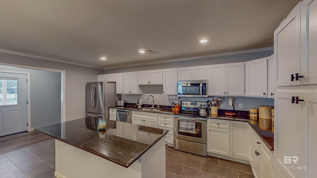 kitchen with white cabinets, appliances with stainless steel finishes, a kitchen island, and dark stone countertops