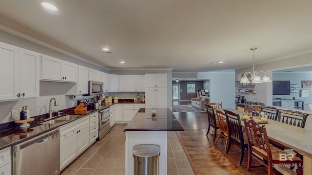 kitchen featuring appliances with stainless steel finishes, decorative light fixtures, a kitchen island, white cabinets, and sink