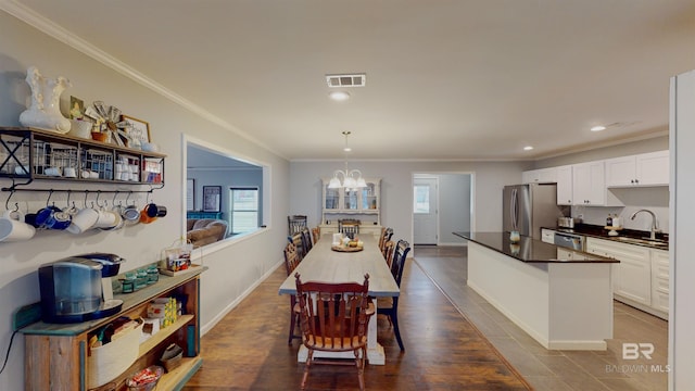 dining area featuring sink, hardwood / wood-style floors, ornamental molding, and an inviting chandelier