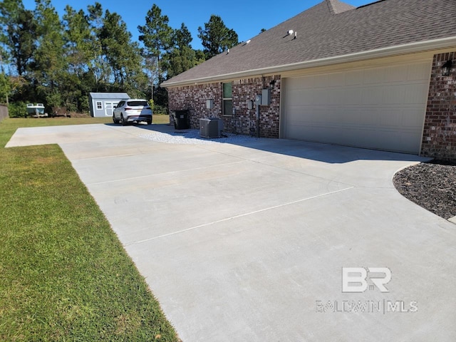 view of side of property with central air condition unit, roof with shingles, brick siding, a yard, and concrete driveway