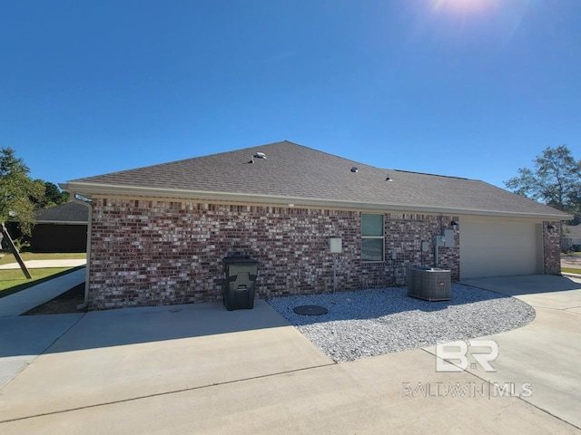 exterior space featuring driveway, roof with shingles, brick siding, and a garage