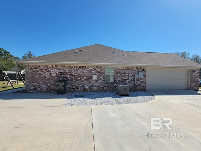 view of property exterior featuring a garage, central air condition unit, concrete driveway, brick siding, and roof with shingles