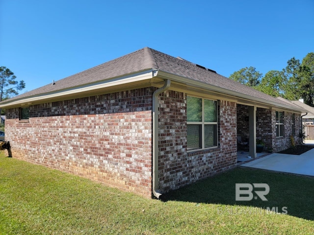 view of property exterior featuring a yard, a patio area, roof with shingles, and brick siding