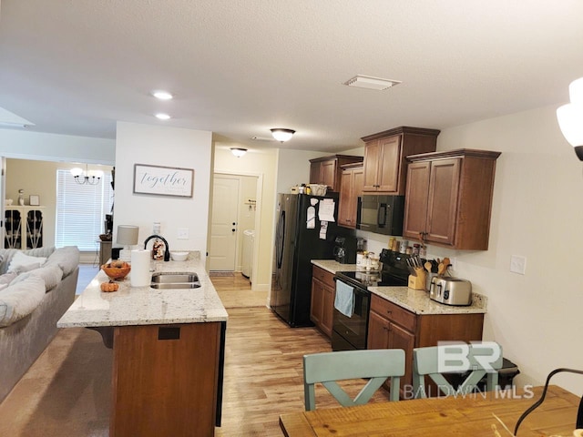 kitchen featuring a peninsula, light wood finished floors, a sink, a kitchen breakfast bar, and black appliances
