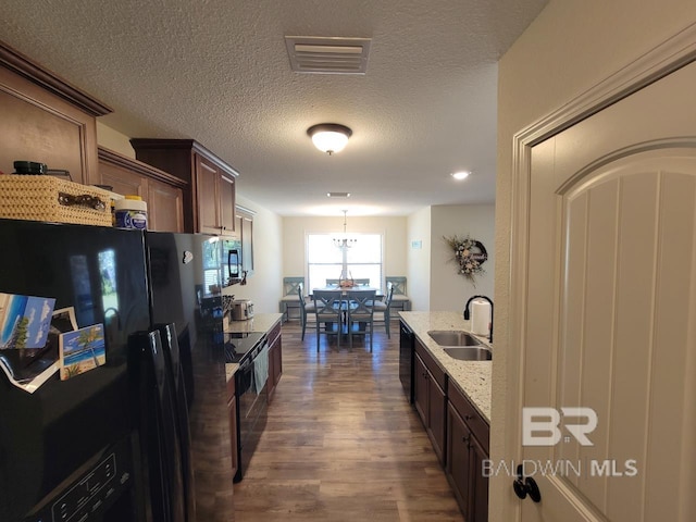 kitchen featuring light stone counters, a sink, dark brown cabinetry, black appliances, and dark wood-style floors
