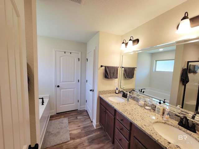 full bathroom with double vanity, a garden tub, wood finished floors, and a sink