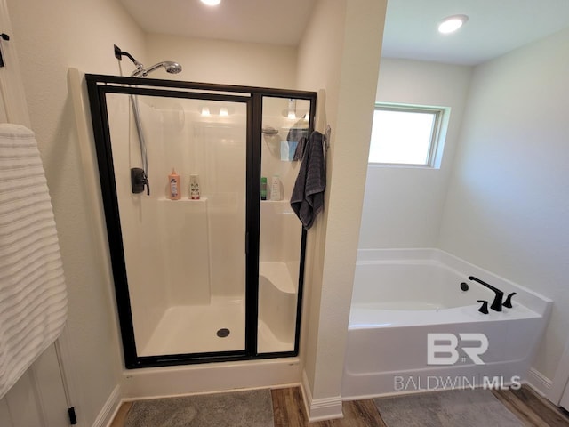 bathroom with a stall shower, a bath, and wood finished floors