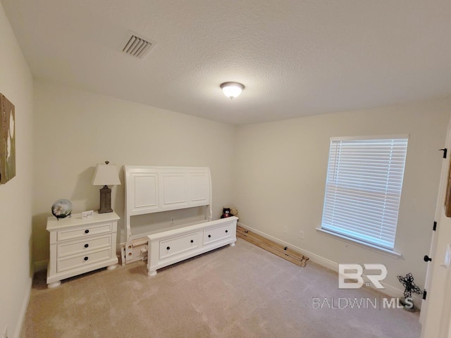 bedroom with baseboards, light carpet, visible vents, and a textured ceiling