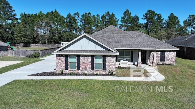 view of front of house featuring board and batten siding, brick siding, fence, covered porch, and a front lawn
