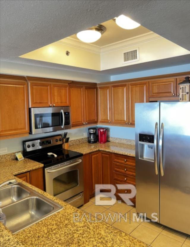 401 E Beach Blvd Unit 507, Gulf Shores, AL 36542 - kitchen with stainless steel appliances, a sink, a tray ceiling, crown molding, and brown cabinetry