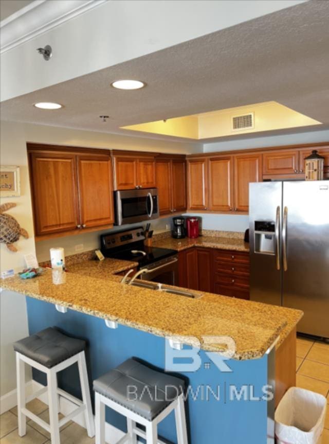 401 E Beach Blvd Unit 507, Gulf Shores, AL 36542 - kitchen with stainless steel appliances, a peninsula, brown cabinets, light stone counters, and recessed lighting