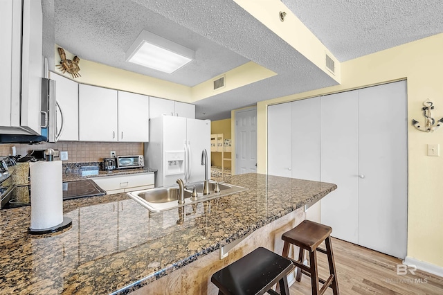 24114 Perdido Beach Blvd Unit 402, Orange Beach, AL 36561 - kitchen with a breakfast bar area, light hardwood / wood-style floors, white fridge with ice dispenser, a textured ceiling, and white cabinets