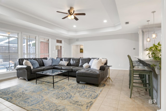 tiled living room with ceiling fan, a tray ceiling, and ornamental molding