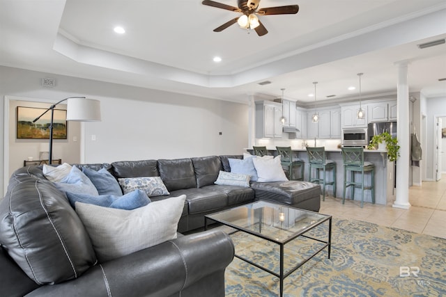 tiled living room with ceiling fan, ornamental molding, and a tray ceiling