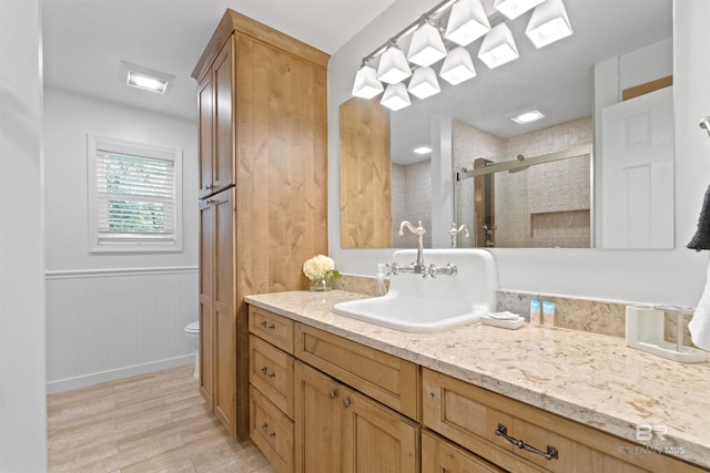 bathroom featuring vanity, a stall shower, toilet, a wainscoted wall, and wood finished floors